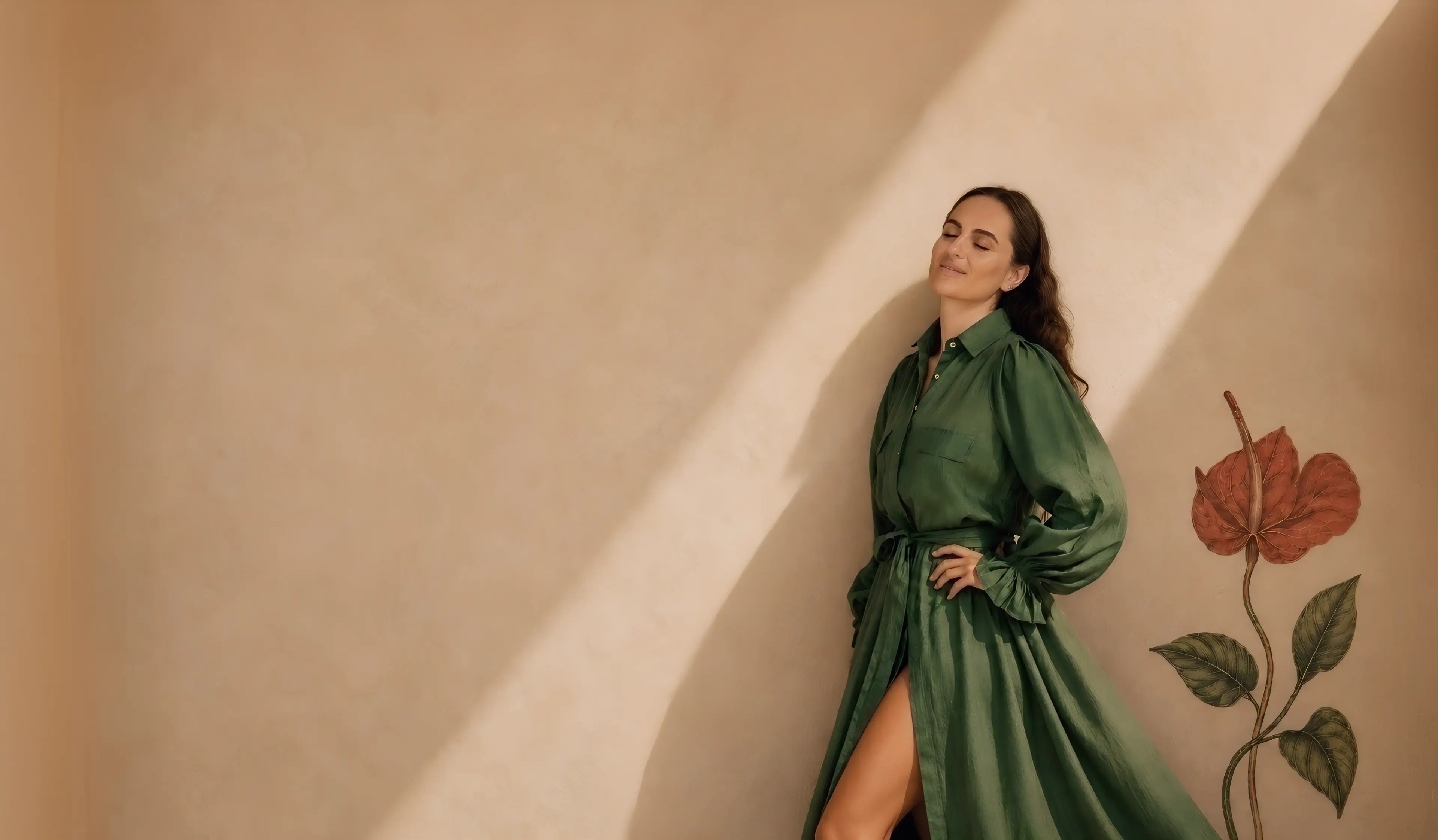 Daria in a green linen wrap dress leaning on a sunlit plaster wall painted with a red anthurium